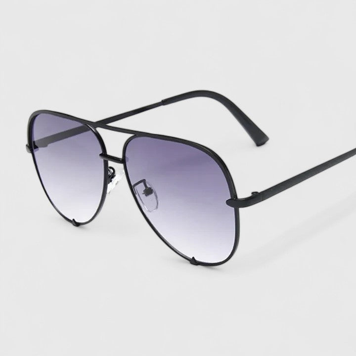 A woman by the sea wearing aviator sunglasses with gradient mirror lenses, relaxed in the sun.