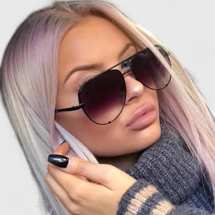A woman by the sea wearing aviator sunglasses with gradient mirror lenses, relaxed in the sun.