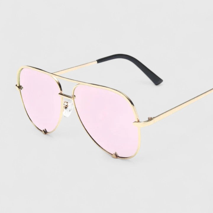 A woman by the sea wearing aviator sunglasses with gradient mirror lenses, relaxed in the sun.