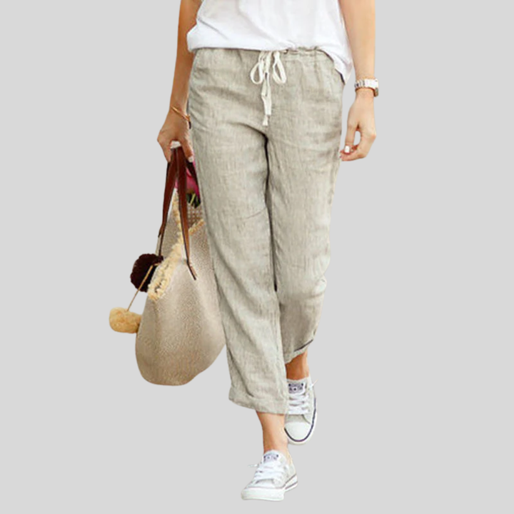 Woman wearing flared drawcord-waist trousers with trainers, walking through town.
