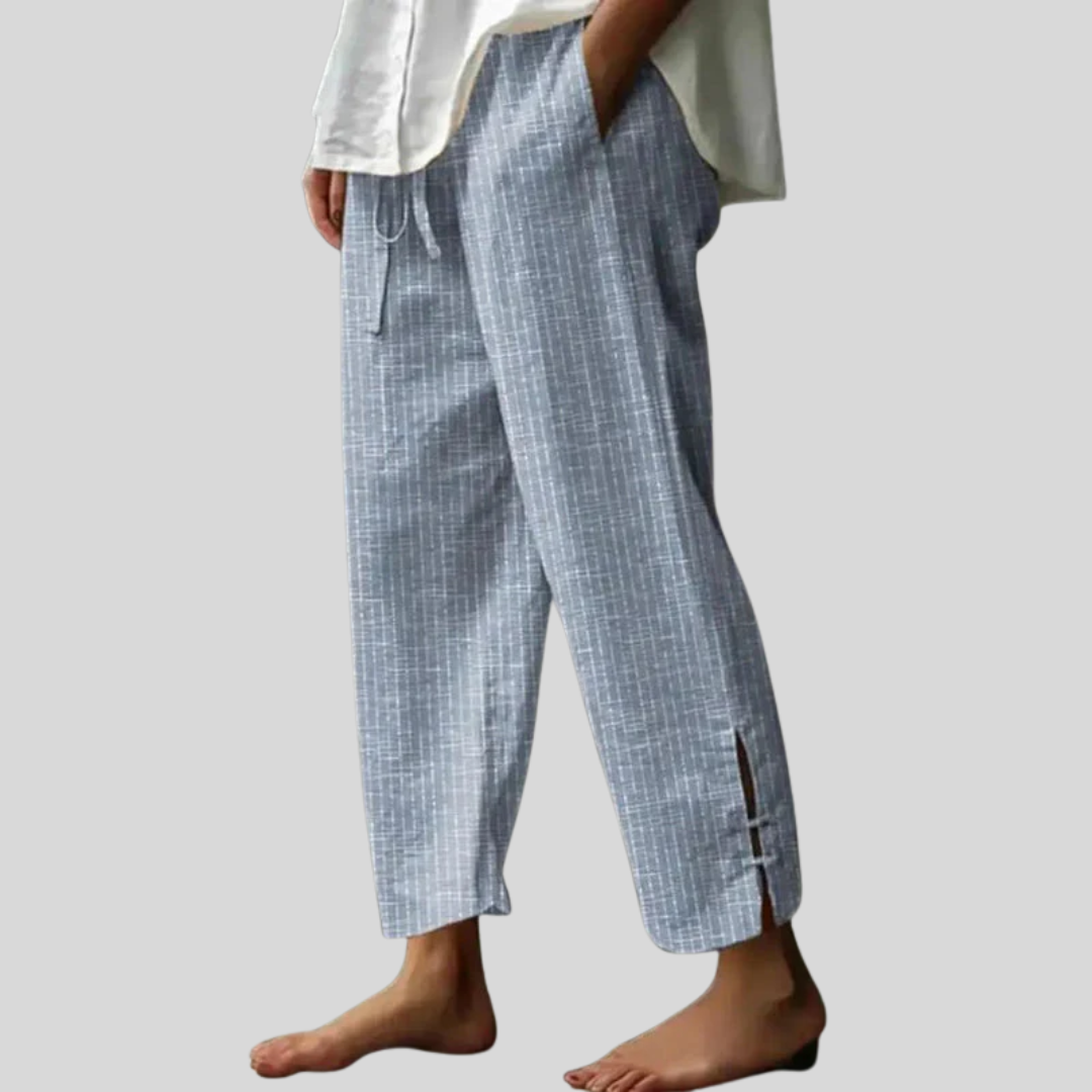 Woman wearing tapered drawcord-waist trousers with sandals, standing in a sunlit garden.