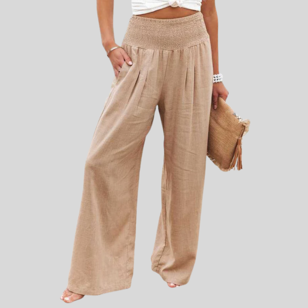 A woman walking by the sea in wide-leg beach trousers with a relaxed, breezy summer look.