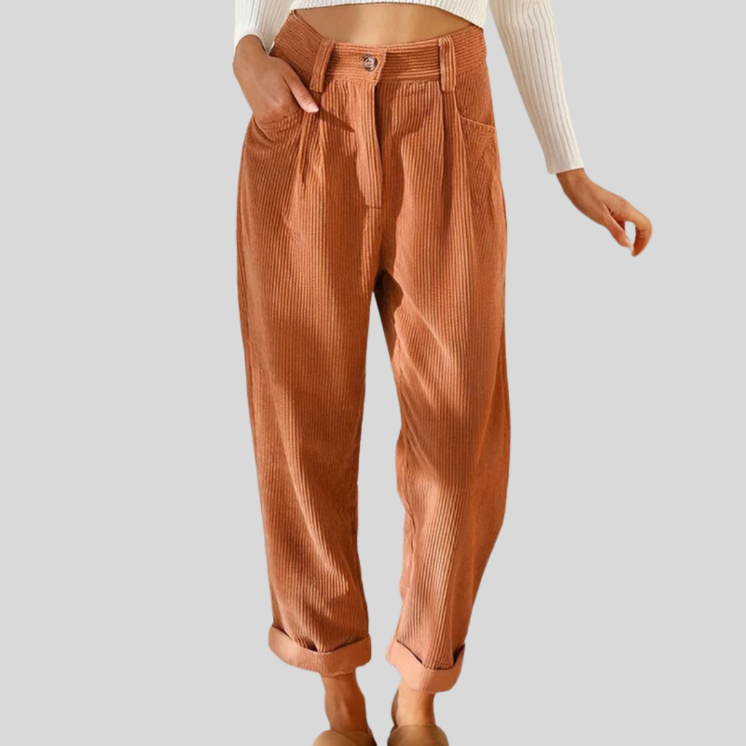 Woman wearing loose high-waisted trousers with a tucked-in top, standing in soft light.