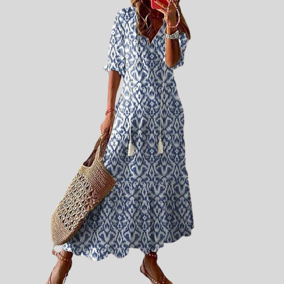 Woman wearing the Colette™ boho maxi dress with fringe details and a V-neckline, relaxed in a warm outdoor setting.