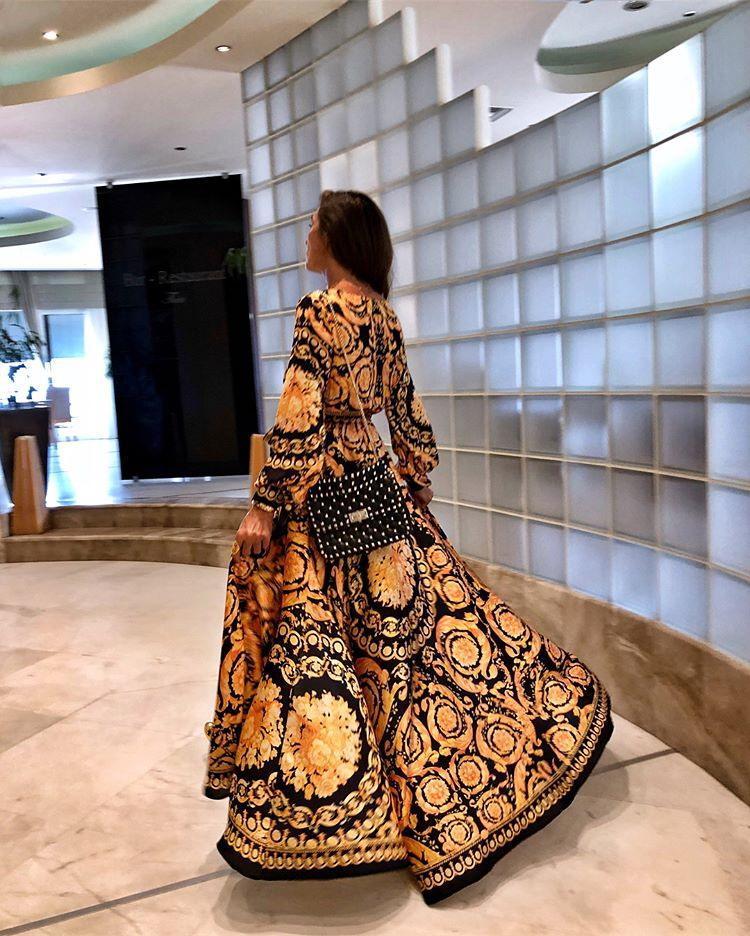 Woman at golden hour wearing the Tessa vintage print maxi dress with a waist belt and long statement sleeves.