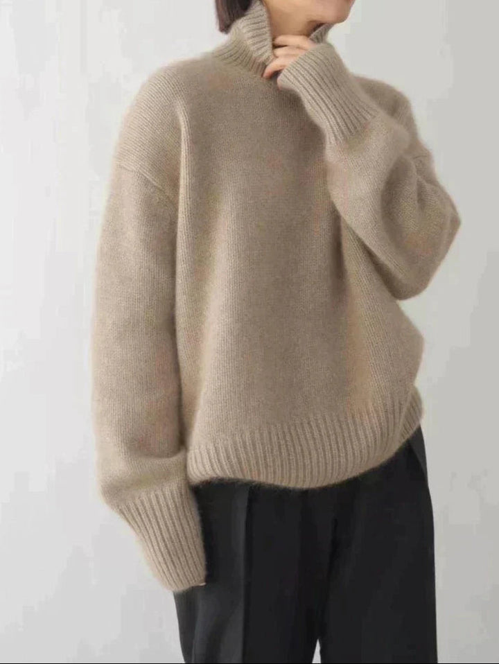 A woman wearing a beige roll-neck jumper, relaxed and warm, paired with trousers.