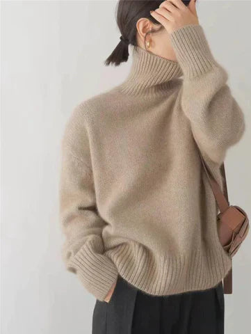 A woman wearing a beige roll-neck jumper, relaxed and warm, paired with trousers.