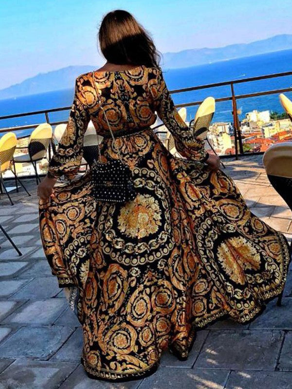 Woman at golden hour wearing the Tessa vintage print maxi dress with a waist belt and long statement sleeves.