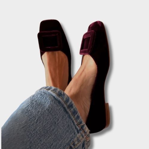 A woman wearing soft, velvety-finish loafers in a rich tone with tailored trousers, looking refined and relaxed.