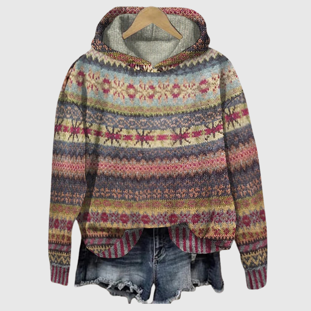 A woman wearing a retro hooded jumper in warm tones with a colourful Nordic pattern.