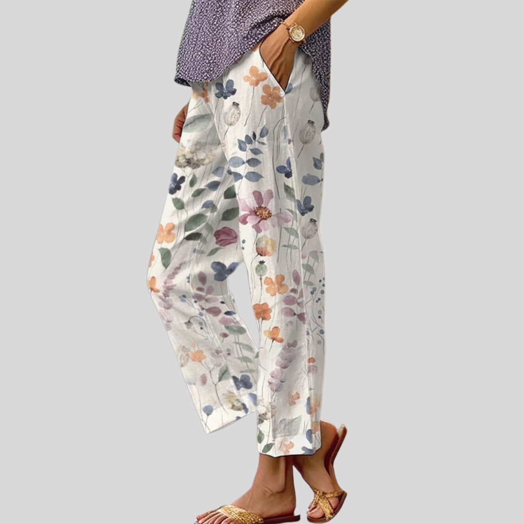 A woman wearing white trousers with a soft watercolour floral print, elastic waist and deep pockets.