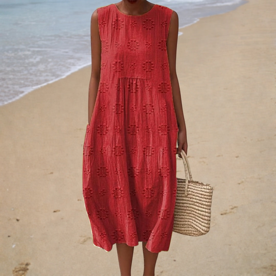 A woman on the beach wearing a red sleeveless summer dress with tonal woven dot detail.