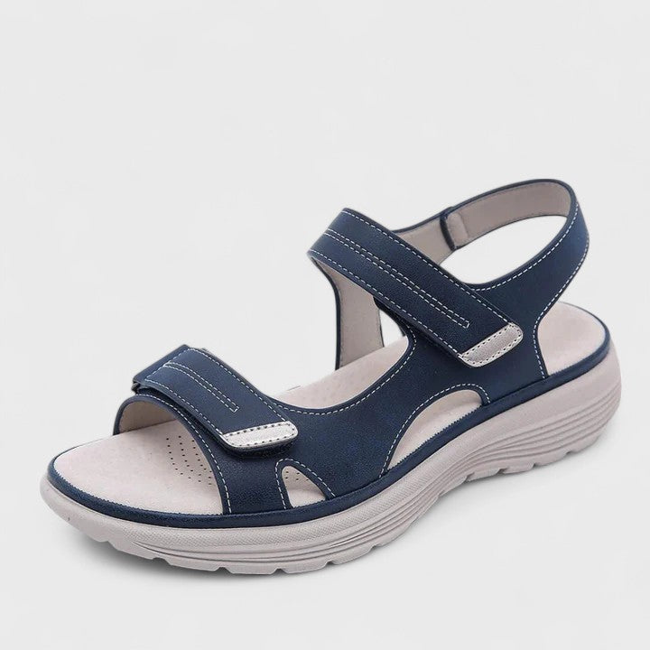 A woman walking gracefully in blue support sandals with a broad, cushioned footbed.