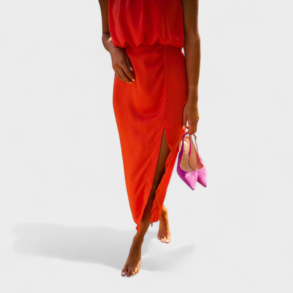 A vivid orange halter-neck fluid midi dress with a front split, styled for a bold summer occasion