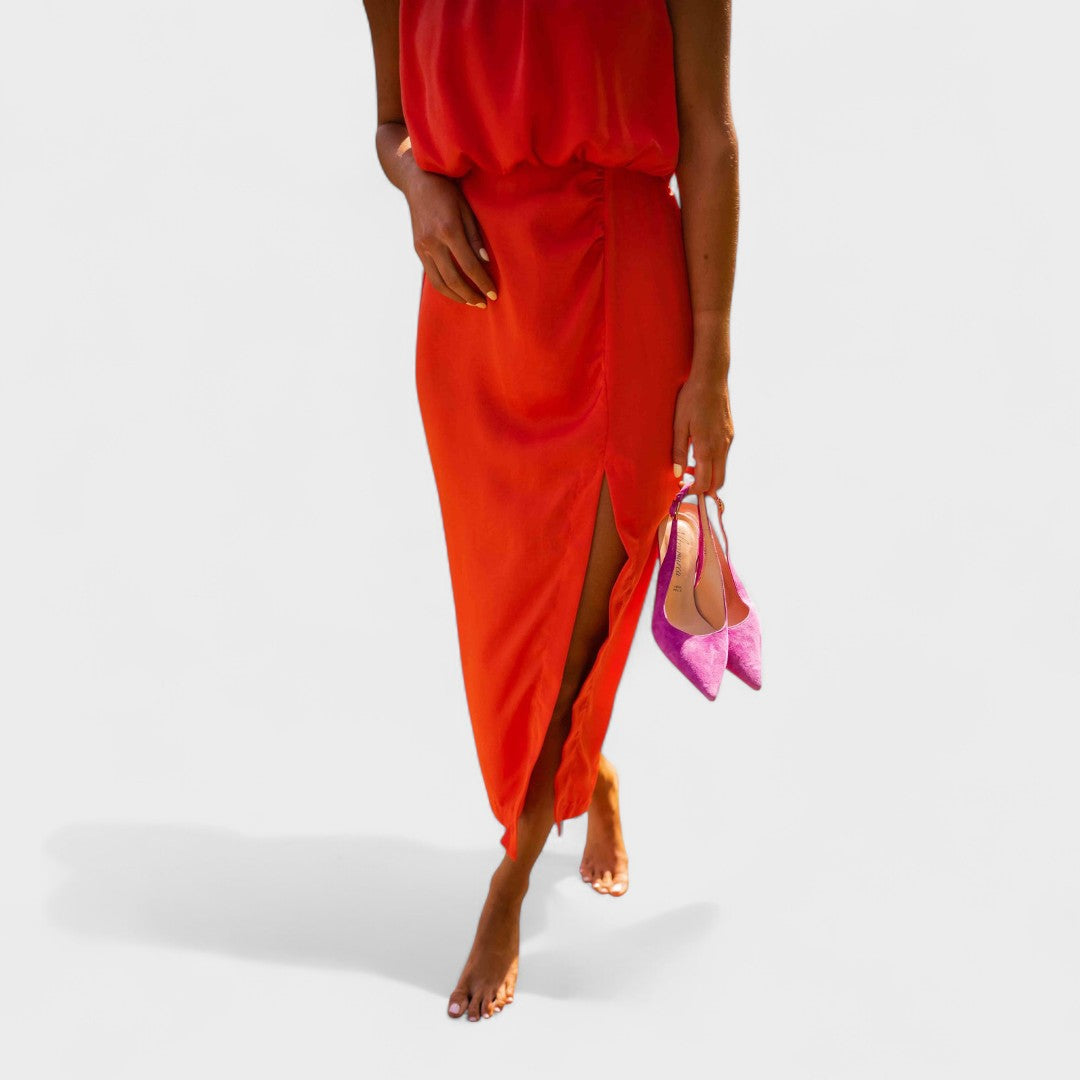 A vivid orange halter-neck fluid midi dress with a front split, styled for a bold summer occasion