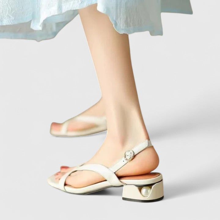 A woman in a white dress wearing minimalist bordeaux strap sandals with a cushioned footbed.