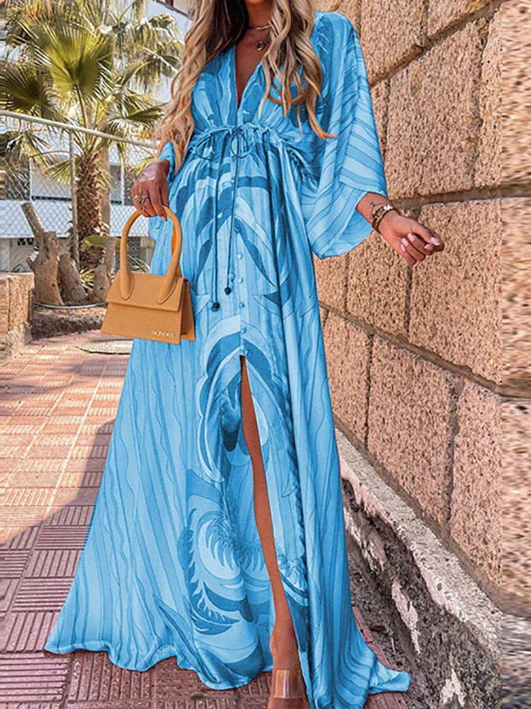 Woman wearing a colourful abstract print kaftan maxi dress with flowing sleeves by the water.