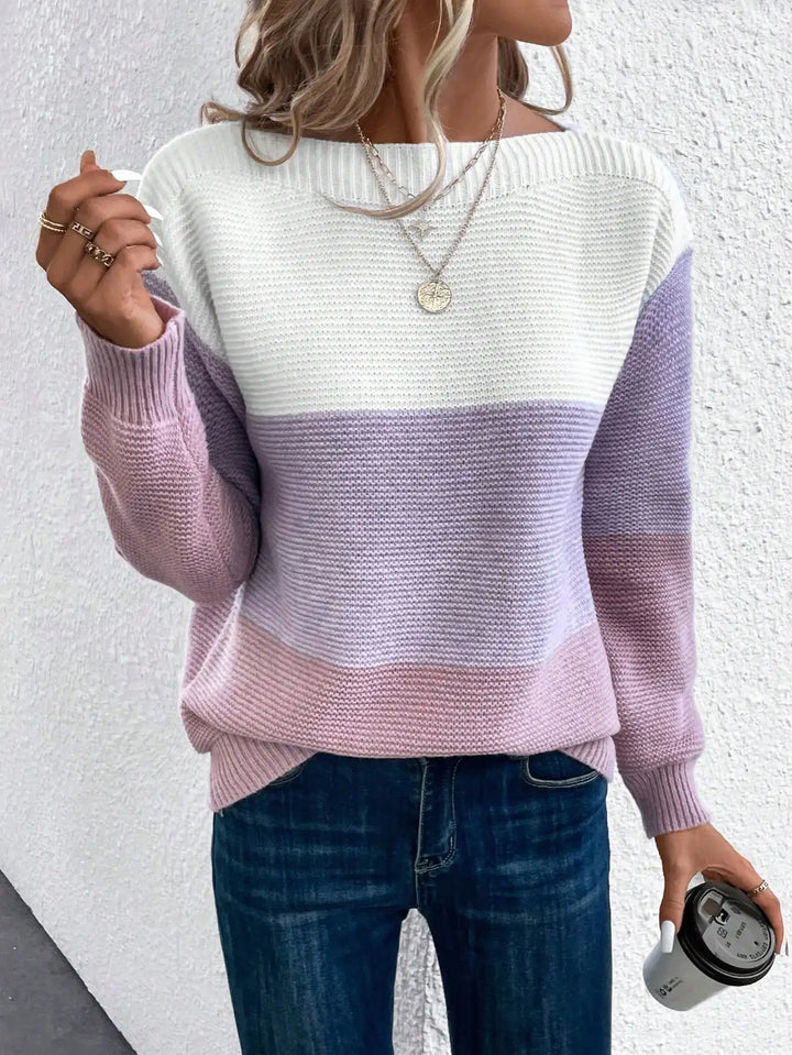 A woman wearing a soft colour block jumper in cream, taupe and beige with a wide boat neckline.