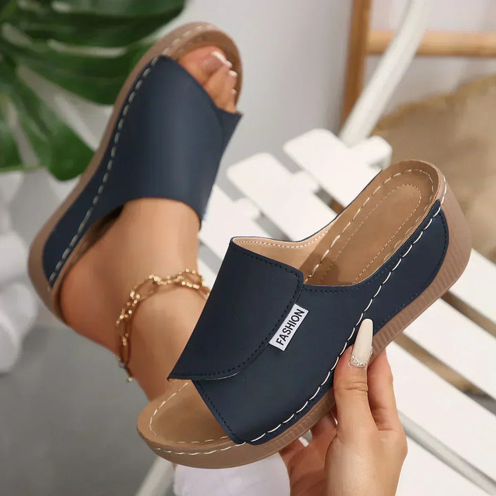 A woman wearing warm tan slide sandals on a sunny seaside walk.