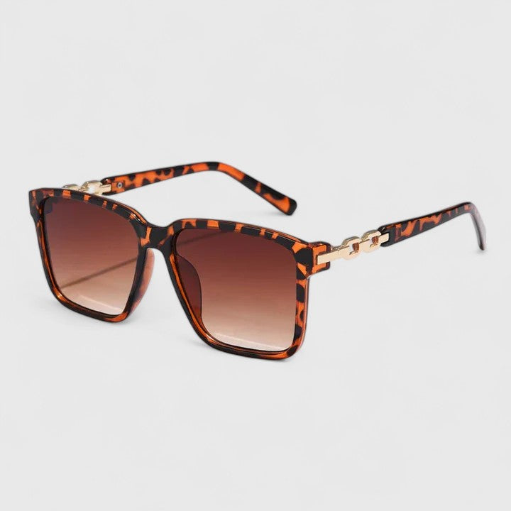 A woman by the pool wearing bold square sunglasses with chain-detail temples, confident in the sun.