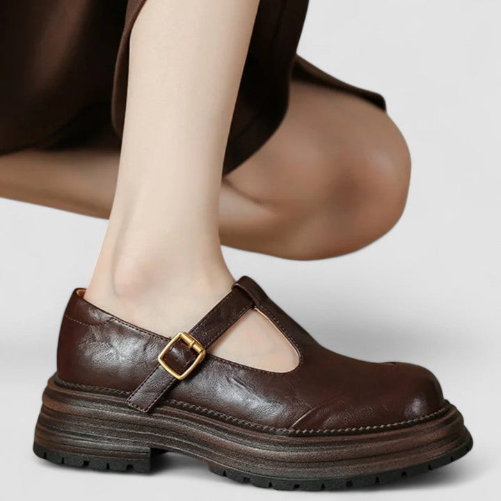 Woman wearing brown Mary Jane comfort shoes with a T-strap, standing on a city footpath.