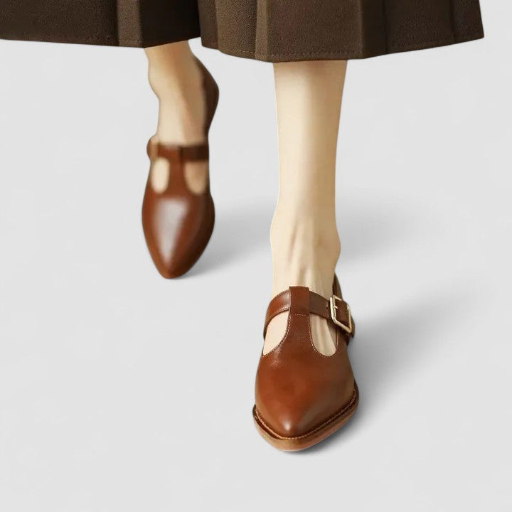 A woman wearing black pointed Mary Jane shoes with an adjustable buckle strap, standing elegantly.