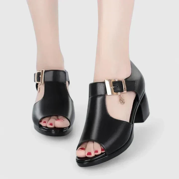 A woman wearing black peep-toe block heels with a T-strap and gold buckle.