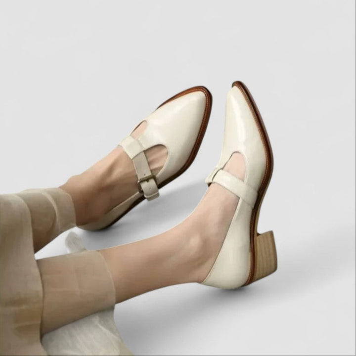 A woman wearing black pointed Mary Jane shoes with an adjustable buckle strap, standing elegantly.