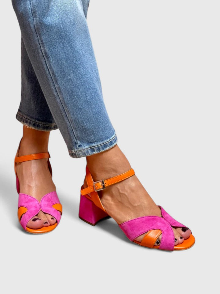 A woman wearing pink and orange open-toe block-heel sandals with an ankle strap, standing comfortably in a summer outfit.