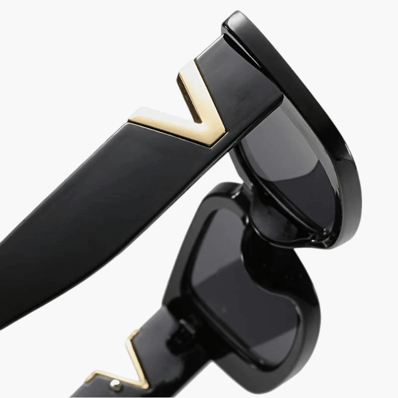 A woman at an outdoor event wearing chunky black rectangular retro sunglasses with a gold-tone accent.