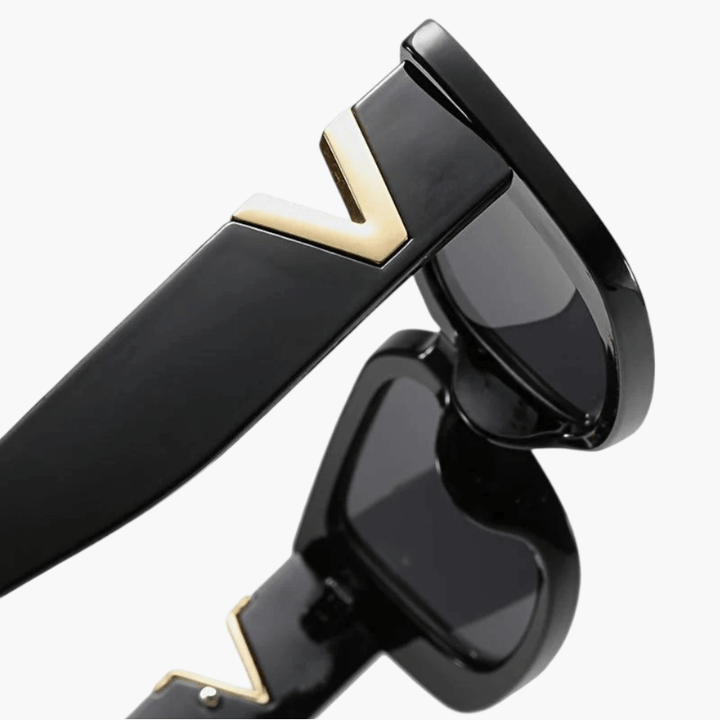 A woman at an outdoor event wearing chunky black rectangular retro sunglasses with a gold-tone accent.