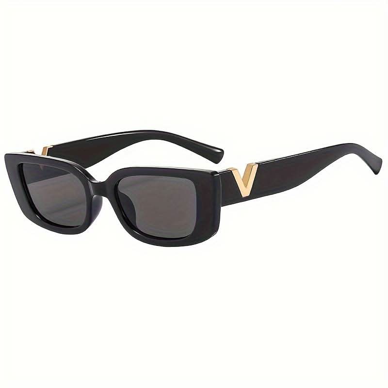 A woman at an outdoor event wearing chunky black rectangular retro sunglasses with a gold-tone accent.