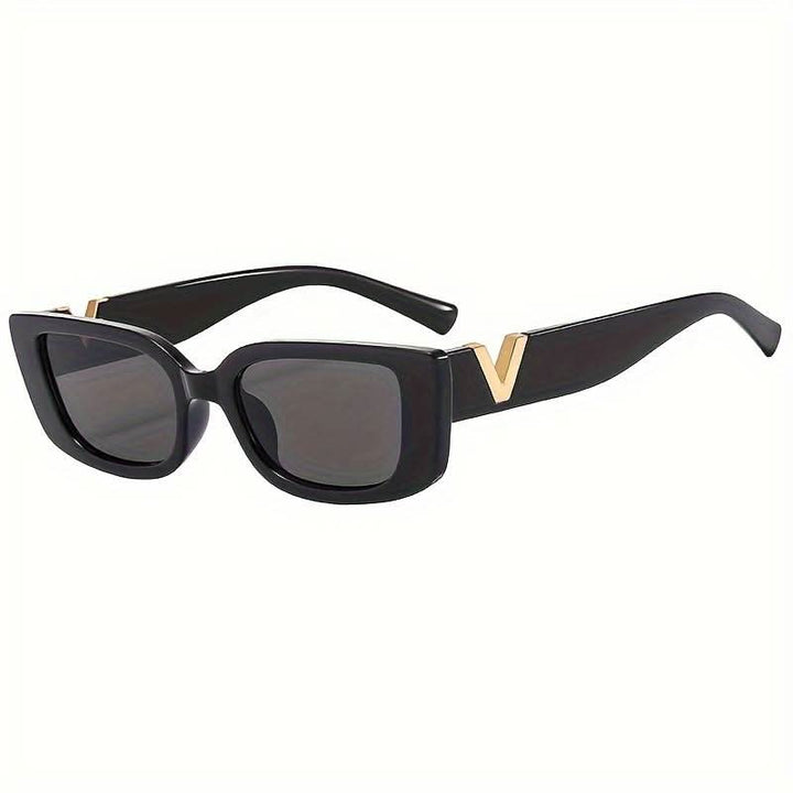 A woman at an outdoor event wearing chunky black rectangular retro sunglasses with a gold-tone accent.