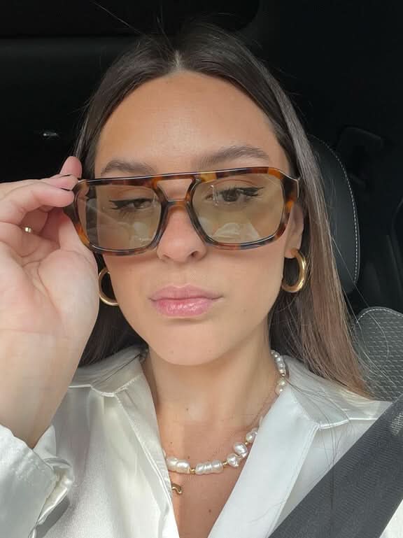 A woman wearing two-tone oval vintage sunglasses on a sunny day outdoors.