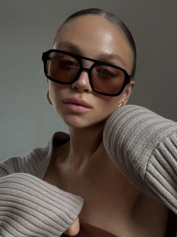A woman wearing two-tone oval vintage sunglasses on a sunny day outdoors.
