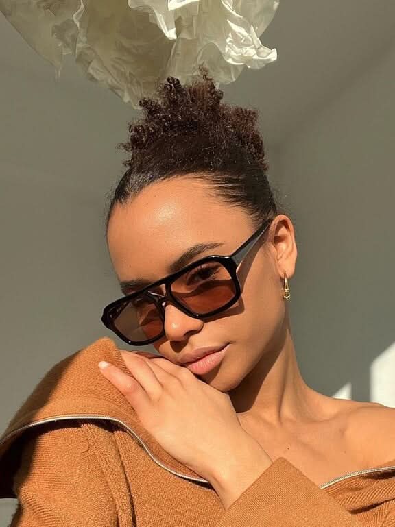 A woman wearing two-tone oval vintage sunglasses on a sunny day outdoors.
