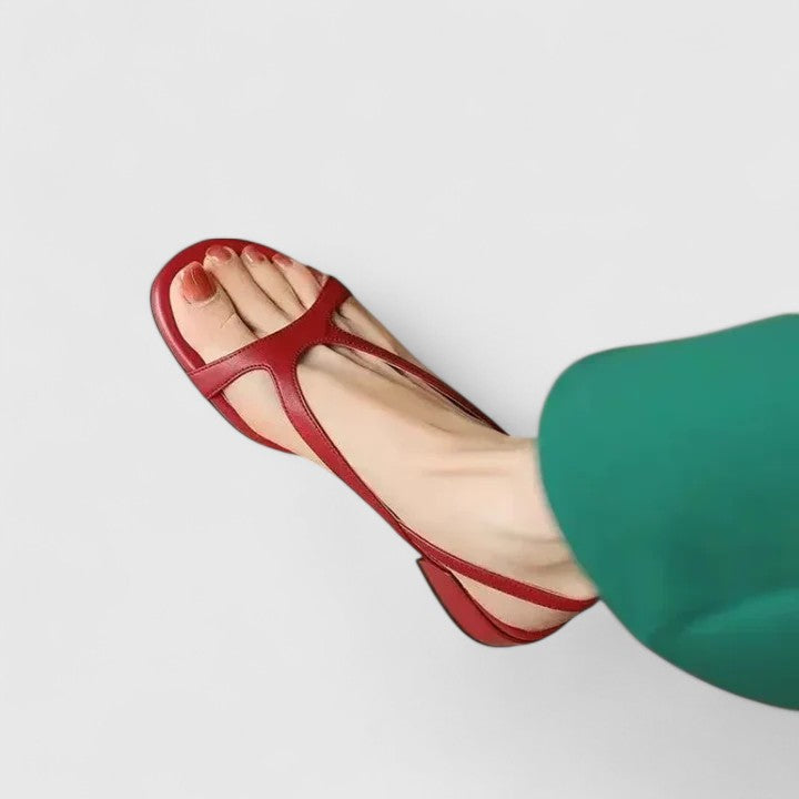 A woman in a white dress wearing minimalist bordeaux strap sandals with a cushioned footbed.
