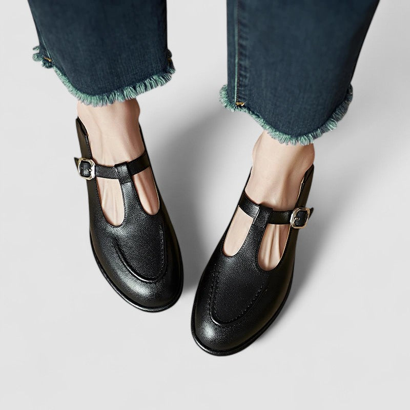 Woman wearing black low-heel Mary Jane shoes with a strap, stepping through a doorway.