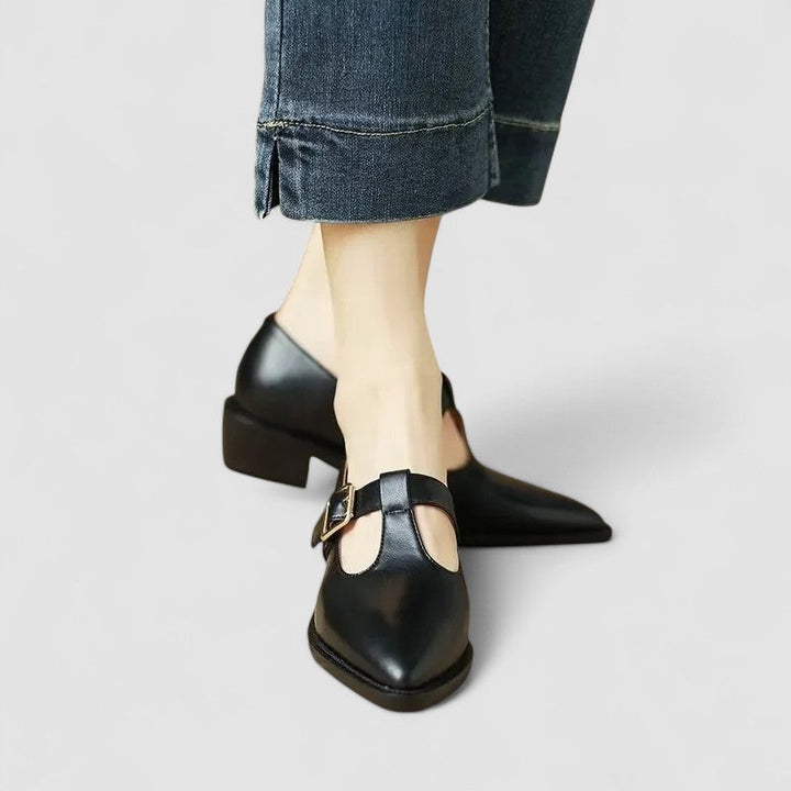 A woman wearing black pointed Mary Jane shoes with an adjustable buckle strap, standing elegantly.