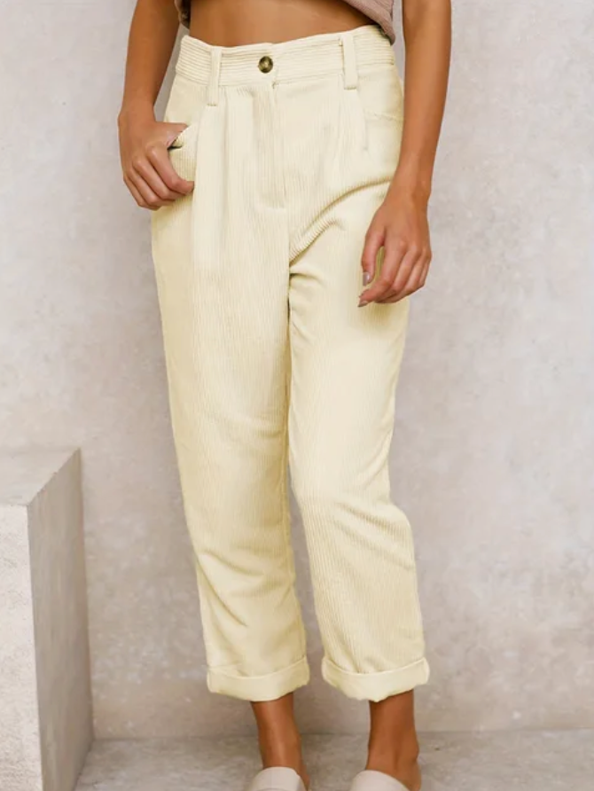 Woman wearing loose high-waisted trousers with a tucked-in top, standing in soft light.