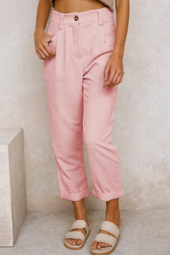 Woman wearing loose high-waisted trousers with a tucked-in top, standing in soft light.