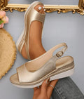 Gold metallic wedge sandals with ankle strap on a neutral background