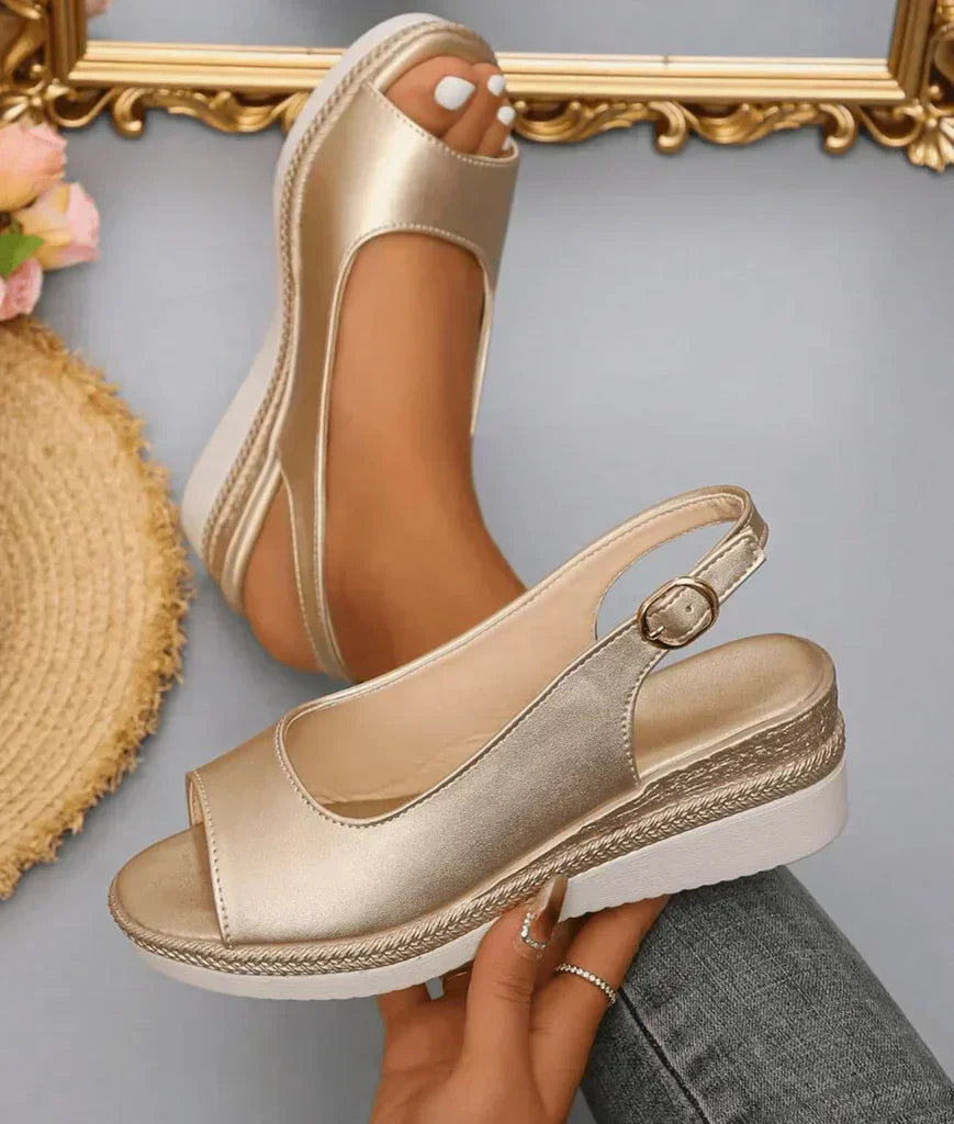 Gold metallic wedge sandals with ankle strap on a neutral background