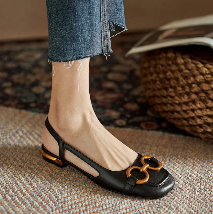 A woman wearing navy square-toe open-back flats with a small golden buckle detail.