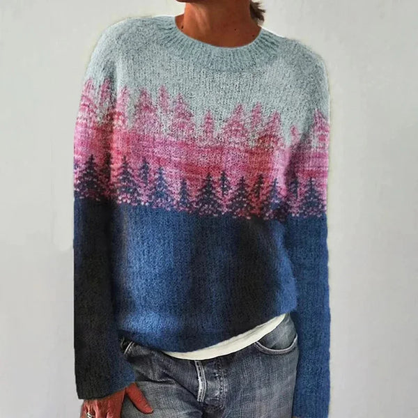 A woman wearing a jumper with a painterly pine forest print in pink, blue and grey, cosy and relaxed for autumn.