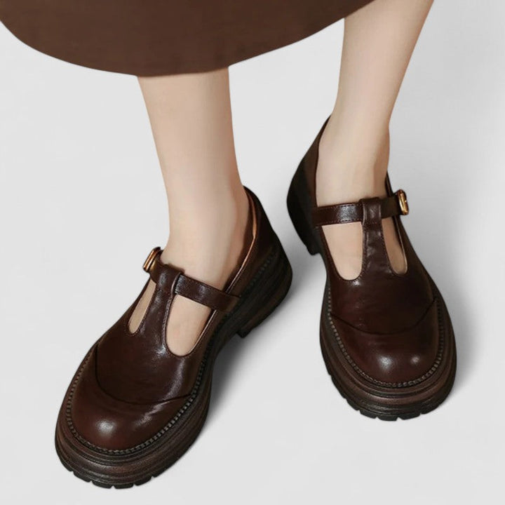 Woman wearing brown Mary Jane comfort shoes with a T-strap, standing on a city footpath.