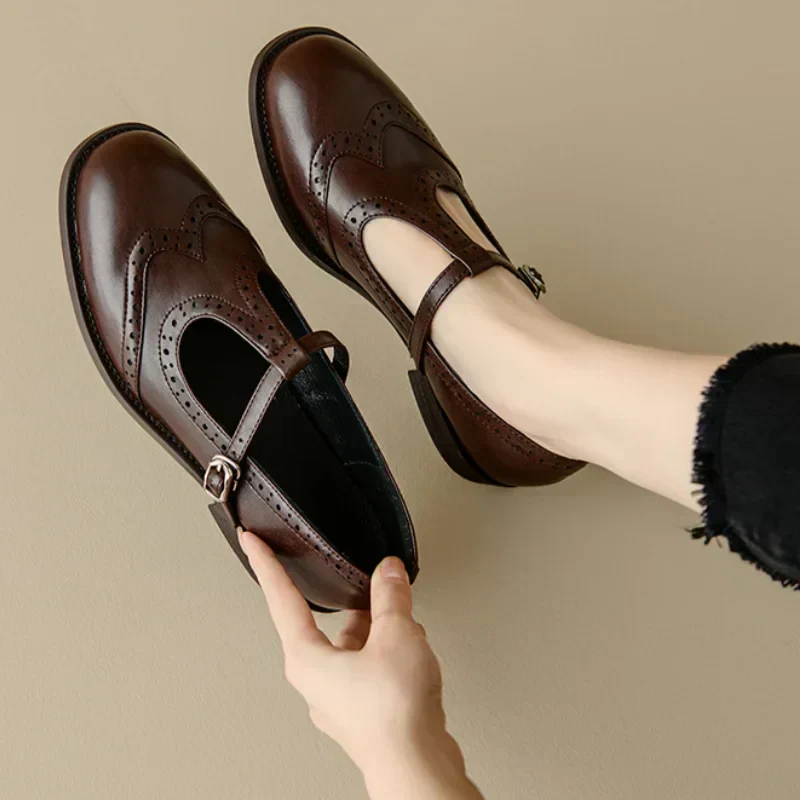 Brown and black Mary Jane shoes with brogue perforations and a T-bar buckle strap