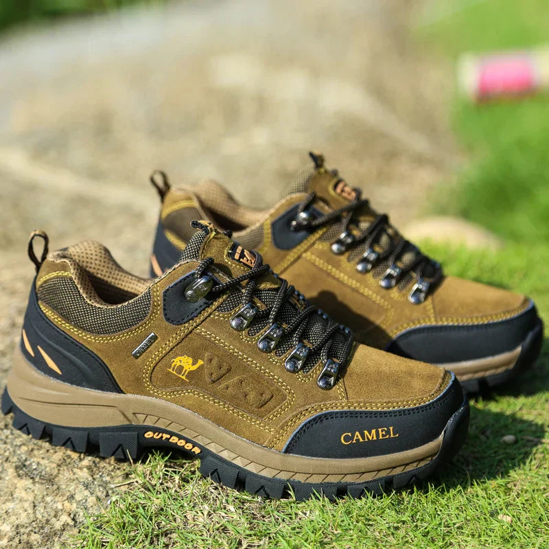 Men's khaki outdoor hiking boot with a rugged sole and lace-up front on a trail setting