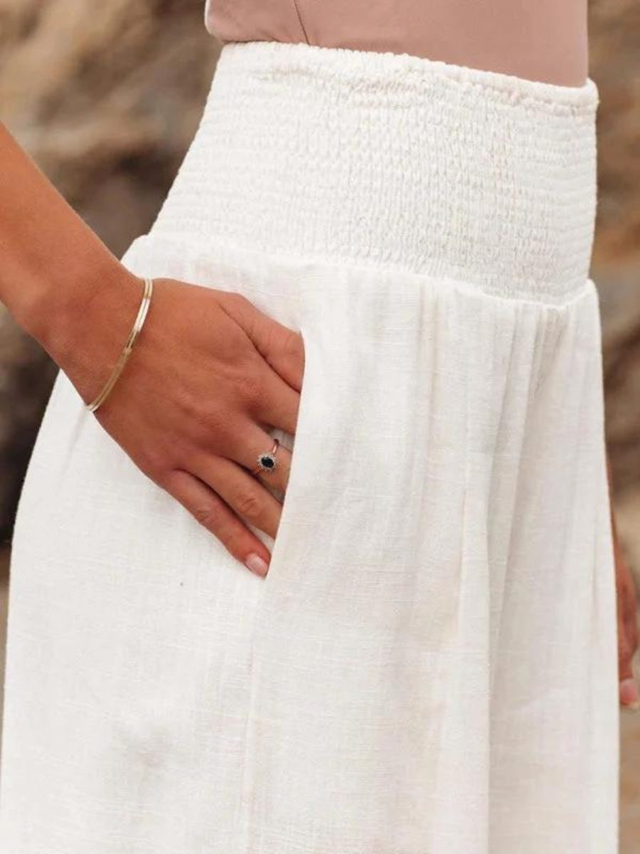 A woman walking by the sea in wide-leg beach trousers with a relaxed, breezy summer look.