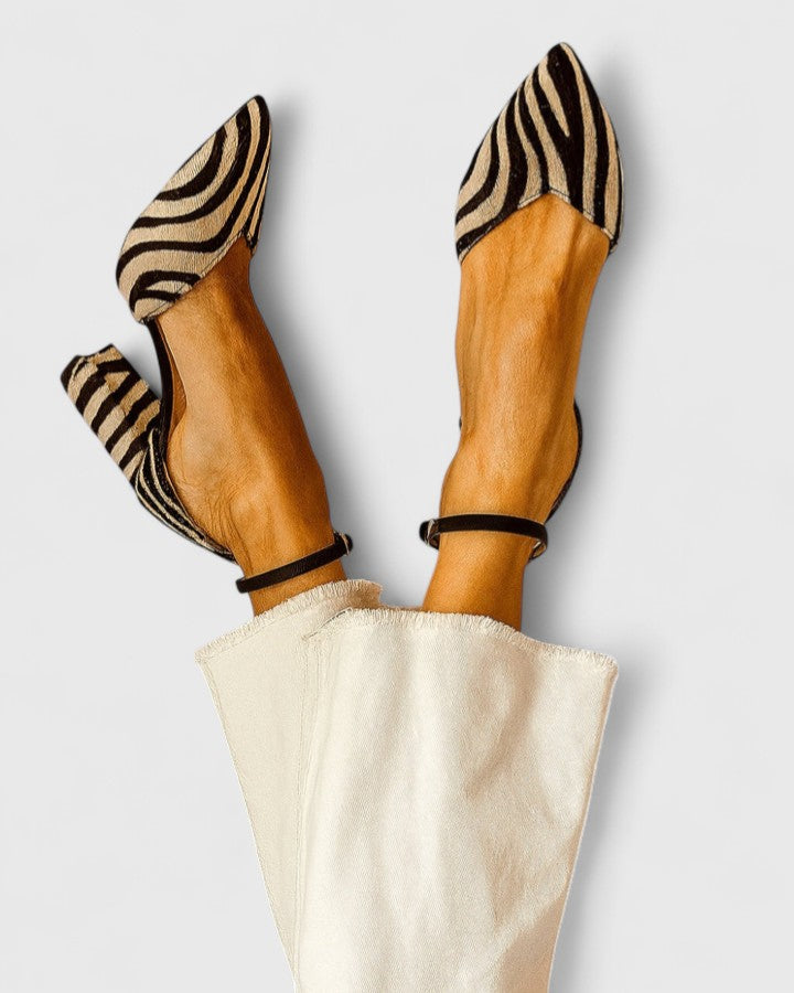 A woman wearing khaki block-heel sandals with an adjustable ankle strap and open design.
